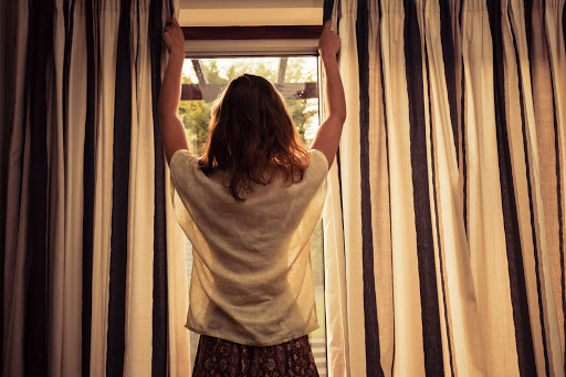 A young woman is opening the curtains at sunrise
