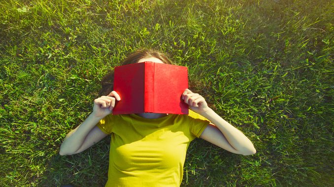 girl reading book lying in warm summer grass. view from above